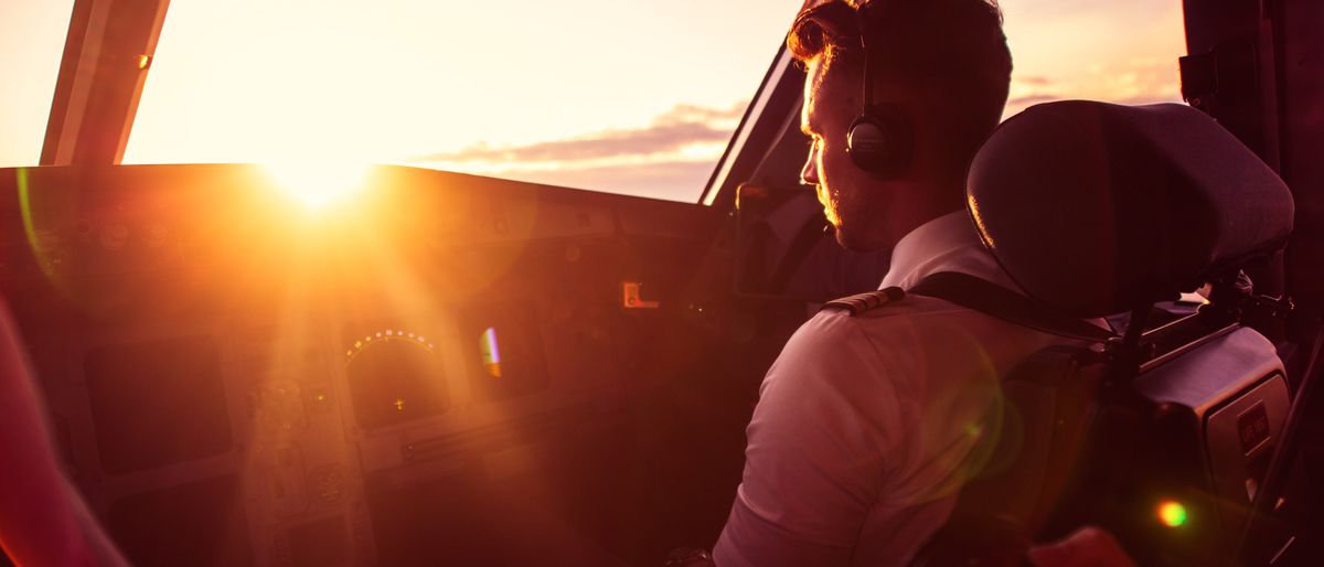 Blick ins Cockpit bei Sonnenaufgang, ein Pilot am Steuer